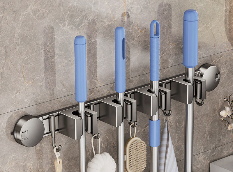 Wall-mounted broom and dustpan holder with blue handles on a tiled wall.