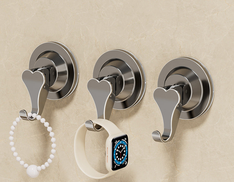 Three metal wall hooks with heart-shaped design on a beige wall.