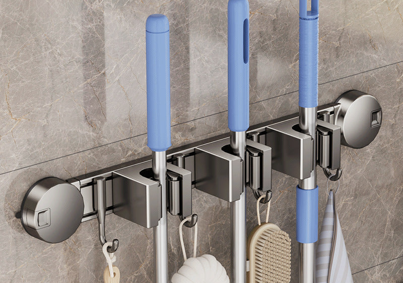 Mop and broom holder with cleaning tools on a tiled wall.